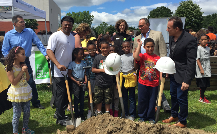 A group of people are standing around a pile of dirt holding shovels.