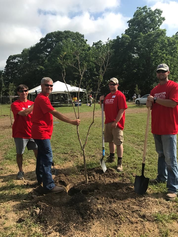 A group of people in red shirts are planting a tree in a field.