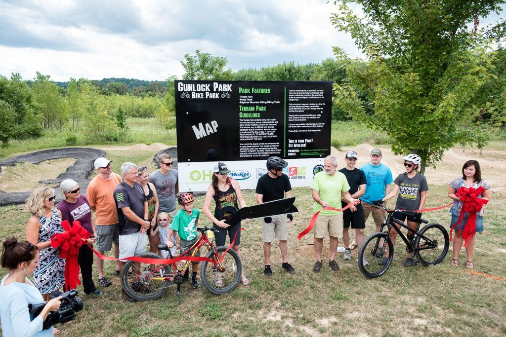 A group of people are standing around a bicycle and cutting a red ribbon.