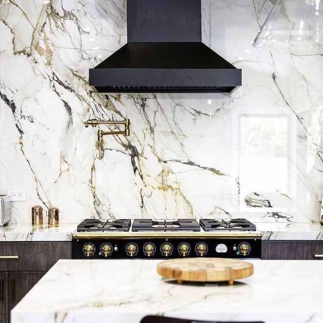 Luxury kitchen featuring elegant marble stone backsplash, modern gas range with gold accents.