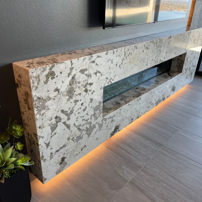 Elegant custom stone fireplace with a sleek design, featuring a glass insert and ambient lighting.
