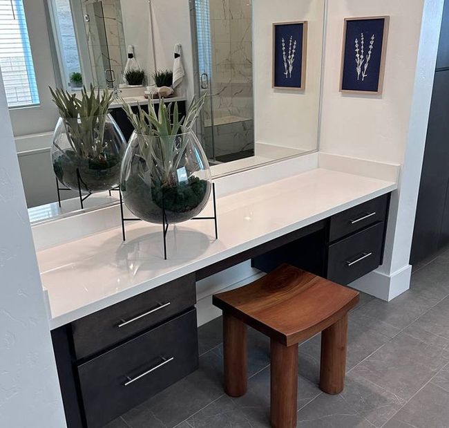 Modern bathroom vanity with white stone countertop, decorative glass planters, and dark cabinetry.