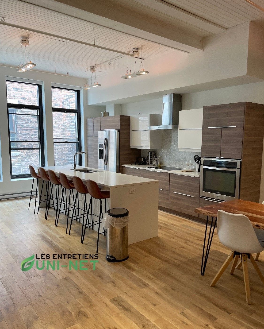 Cuisine moderne avec îlot central, placards marron et crème, parquet et tabourets de bar.