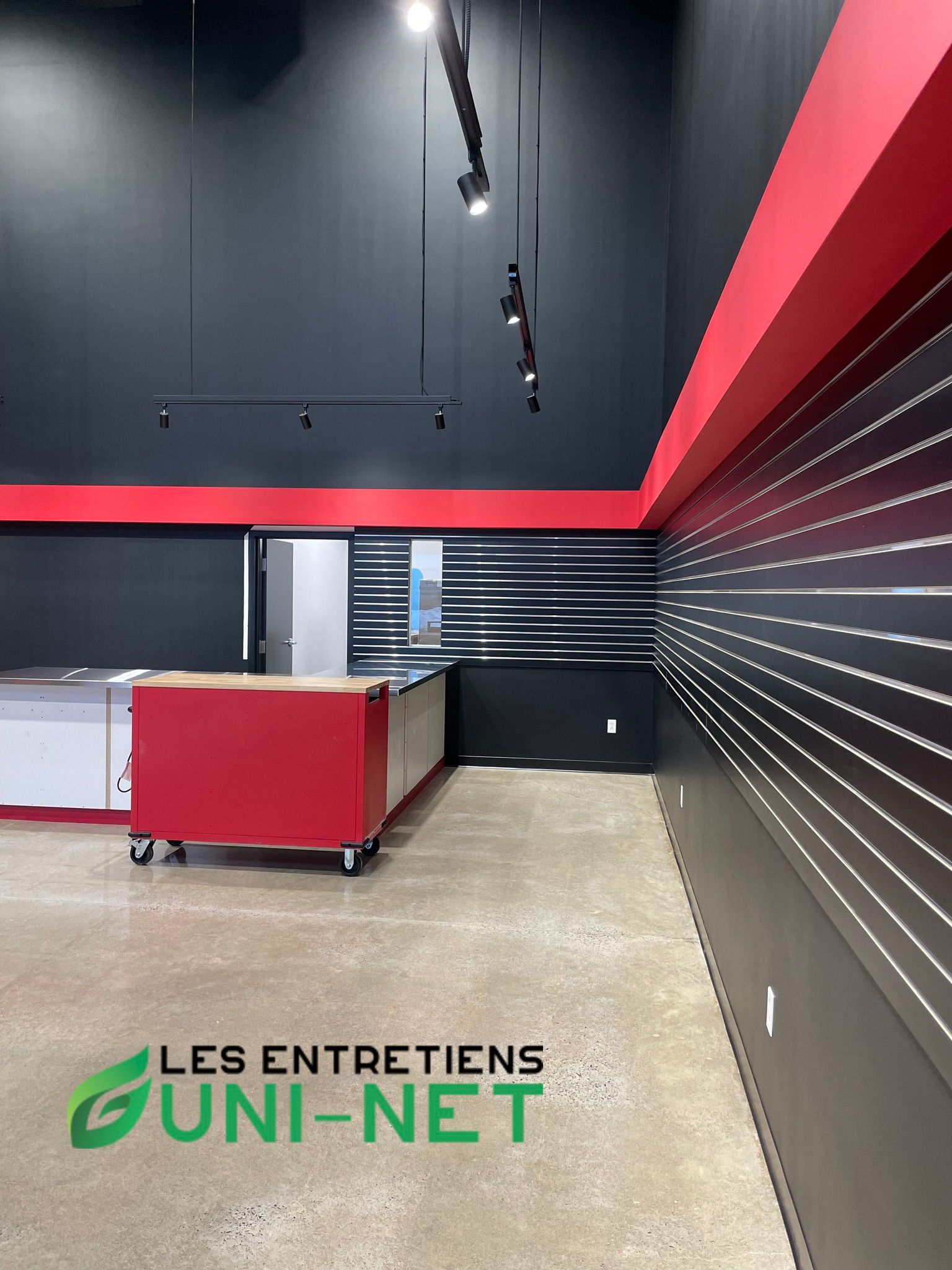 Espace commercial intérieur vide avec murs rouges et noirs, sol en béton et îlot d'exposition.
