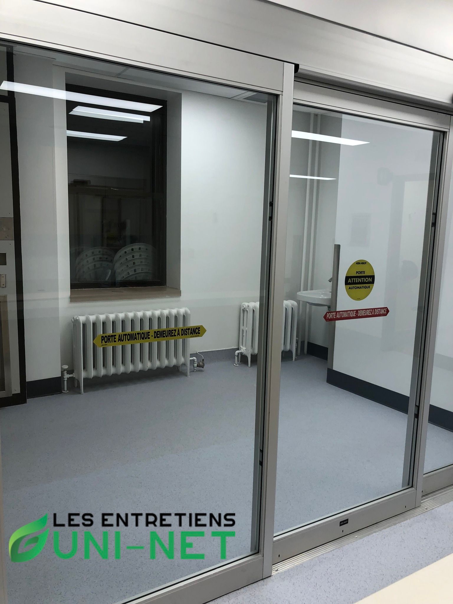 Portes coulissantes en verre, vue intérieure d'une pièce. Sol gris, murs blancs et radiateur sous une fenêtre.