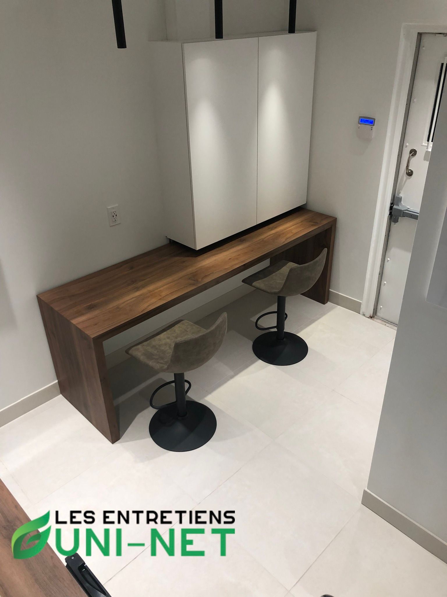 Bar en bois avec deux tabourets contre un mur, surmonté d'un meuble blanc.