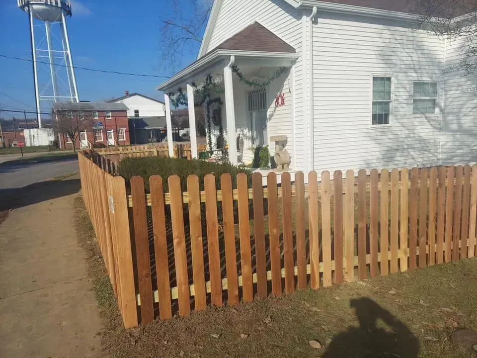 Wooden picket fence in front of a white house with a water tower in the background.