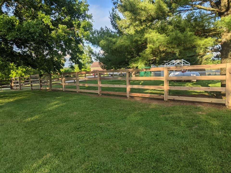 Wooden fence along a grassy lawn, trees in background, sunny day.
