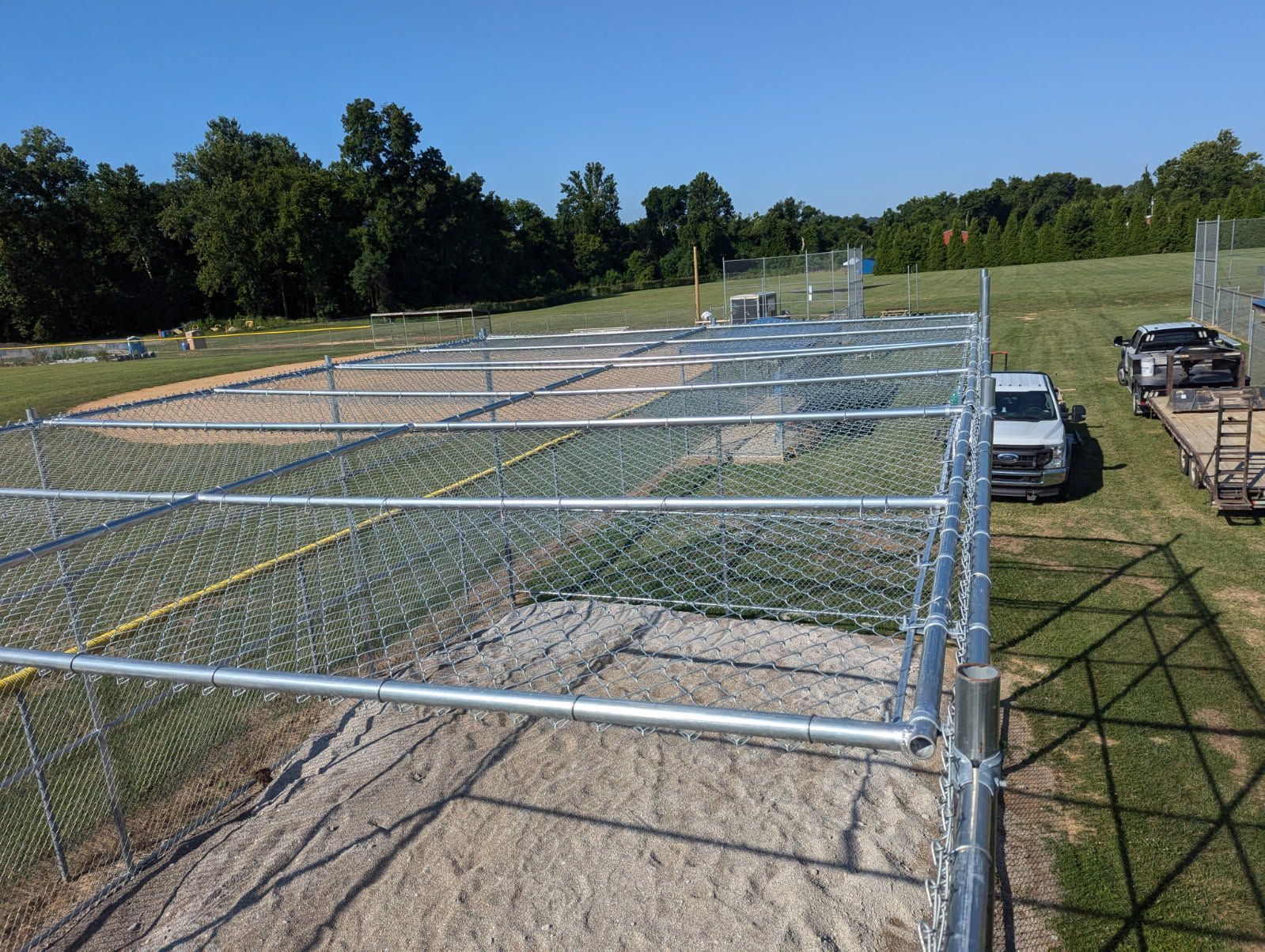 Chain-link fence enclosures in a grassy field, possibly a research area, with a white van parked nearby.