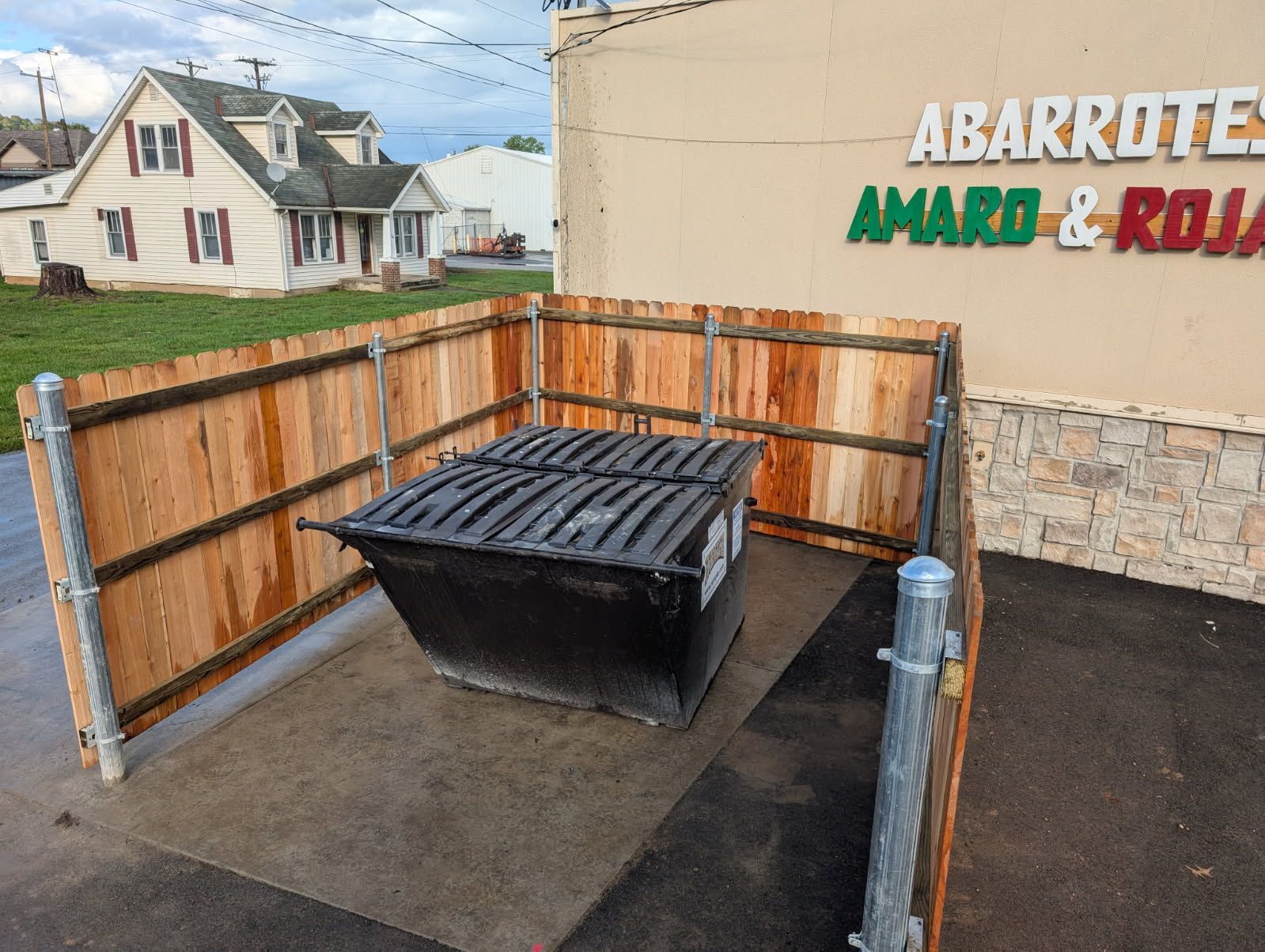 Dumpster enclosed by wooden fencing in front of a store with a sign.