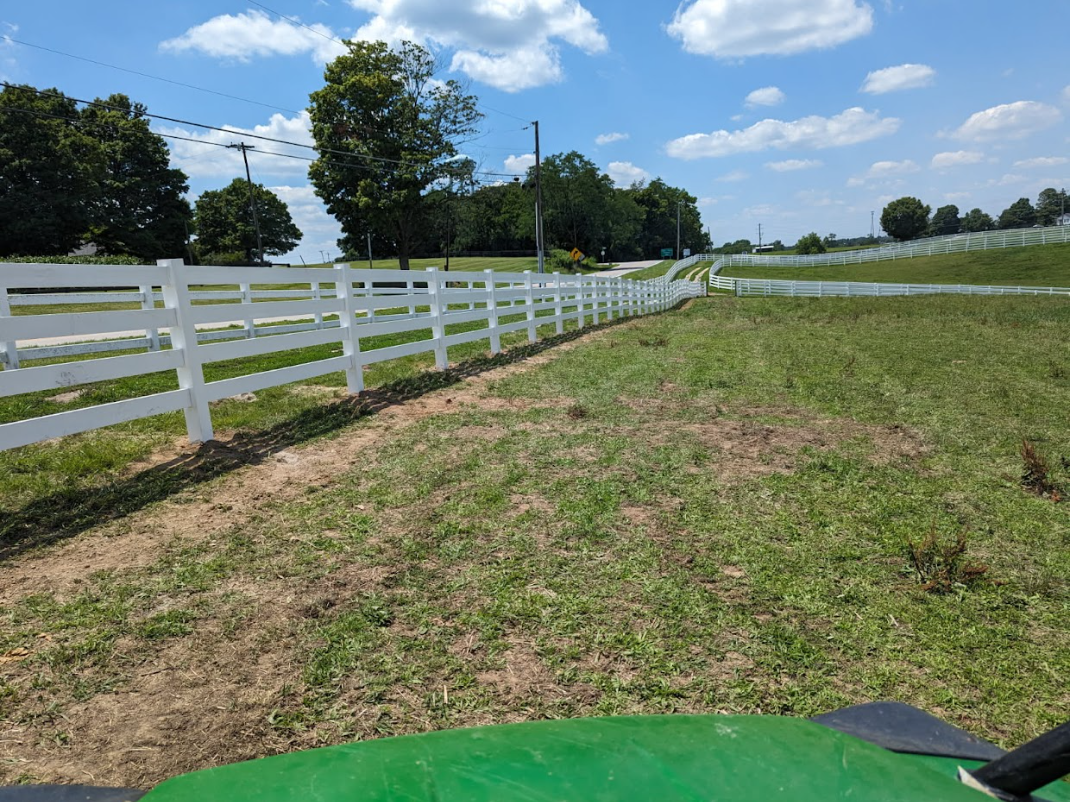 White fence along a grassy field on a sunny day. Green tractor in foreground.