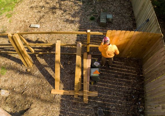Person in orange jacket building wooden fence outdoors.