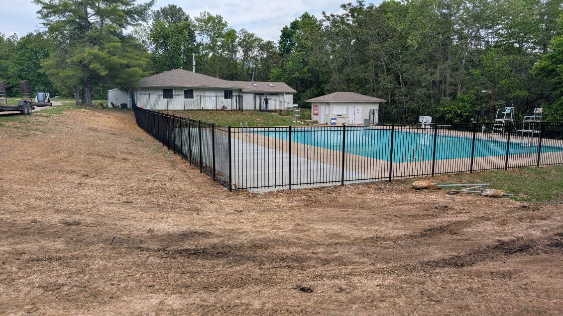 Pool with metal fence, house in background, dirt yard.
