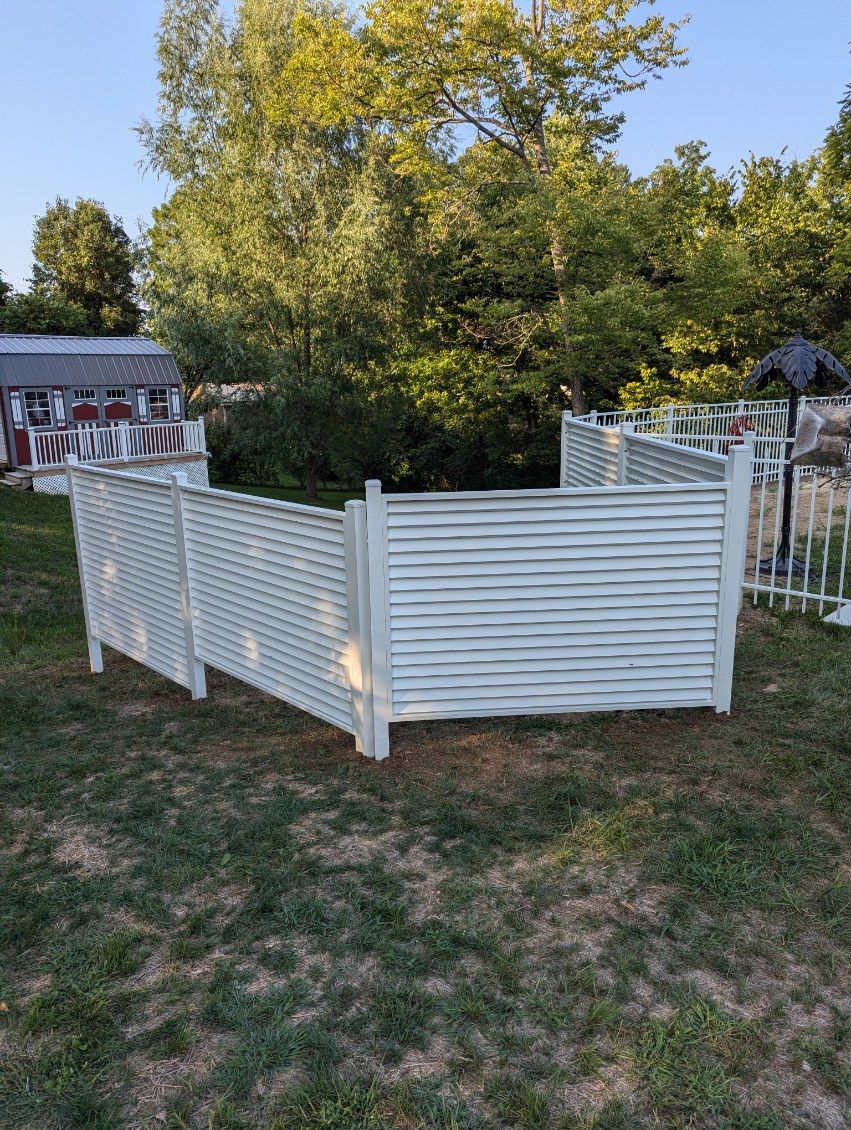 White slatted wooden fence in grassy yard, surrounded by trees.