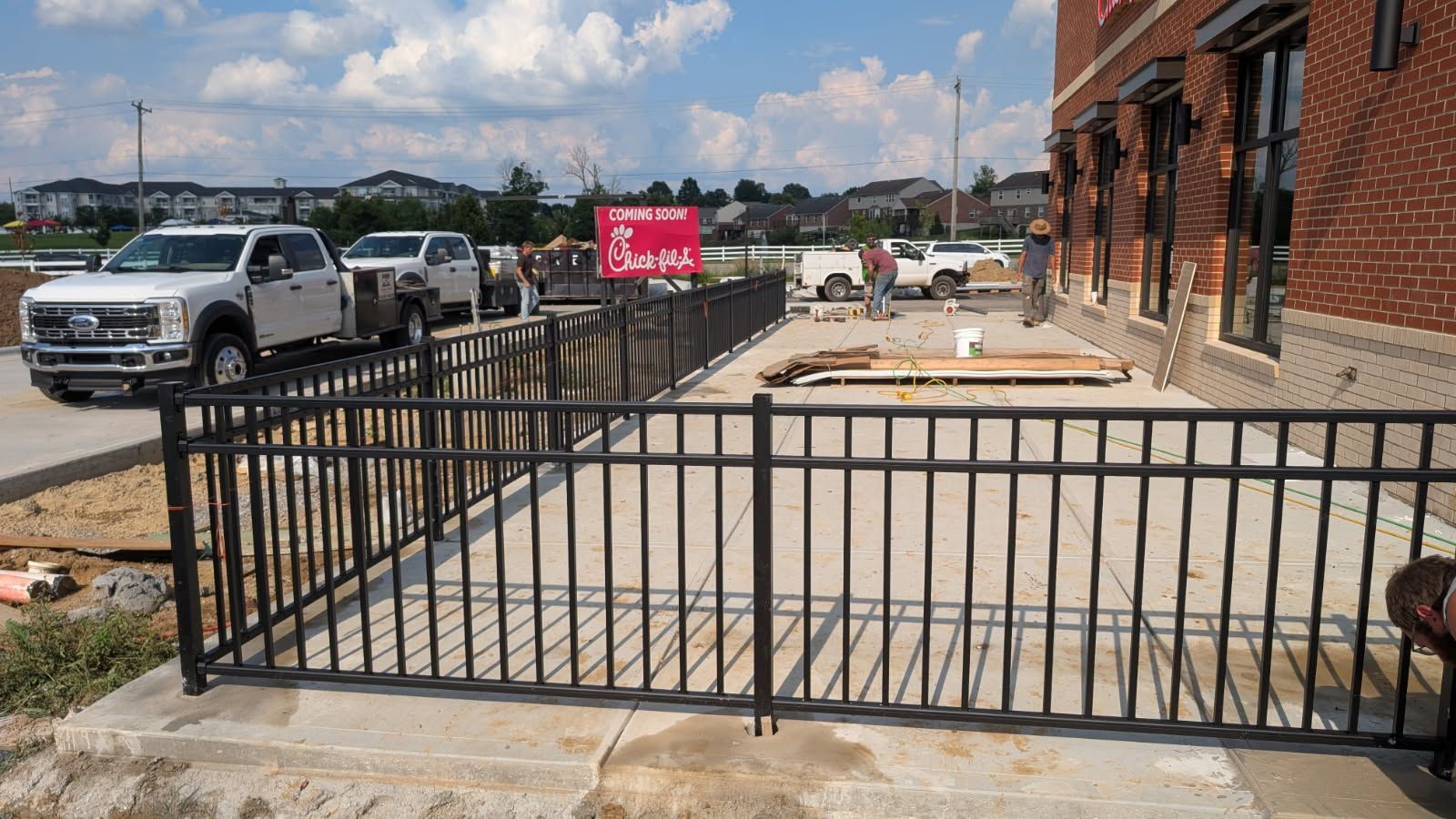 Black metal fence in front of a Chick-fil-A under construction, with trucks and workers present.