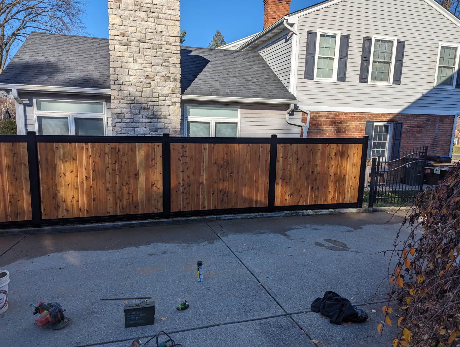 Wooden fence with black frame in front of a house. The fence spans across a driveway.