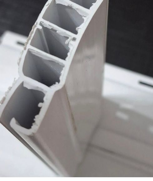 Una persona con uniforme azul está de pie en una sala de estar, ajustando las persianas blancas de una ventana.