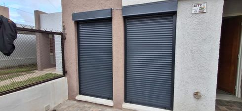 Cuatro estores enrollables de color beige cuelgan de un marco de ventana con molduras de madera