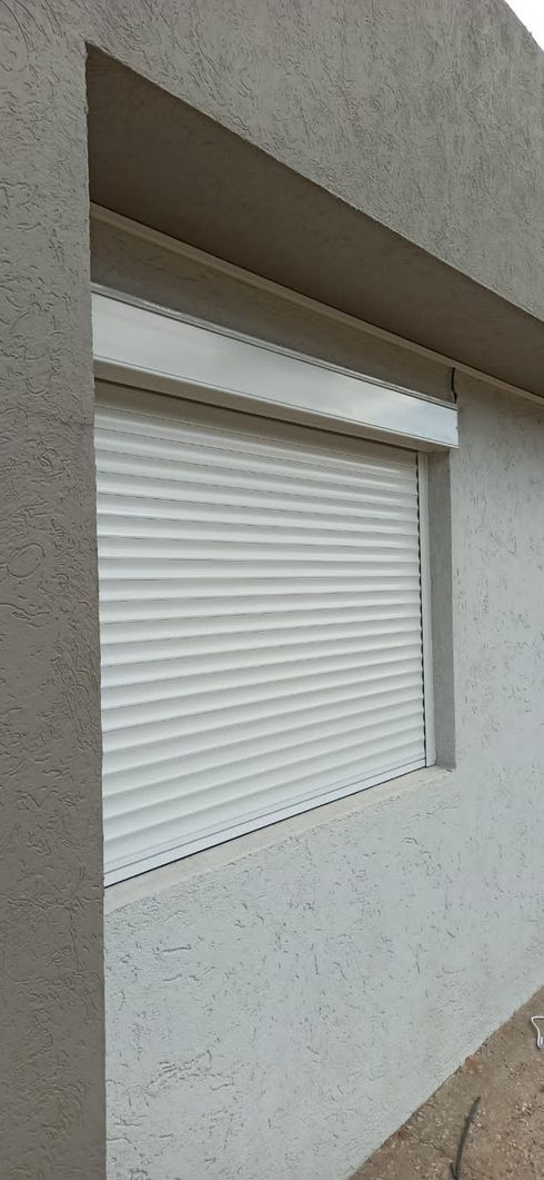 Una ventana de madera parcialmente cubierta por una persiana enrollable blanca y enmarcada por cortinas de lino beige.