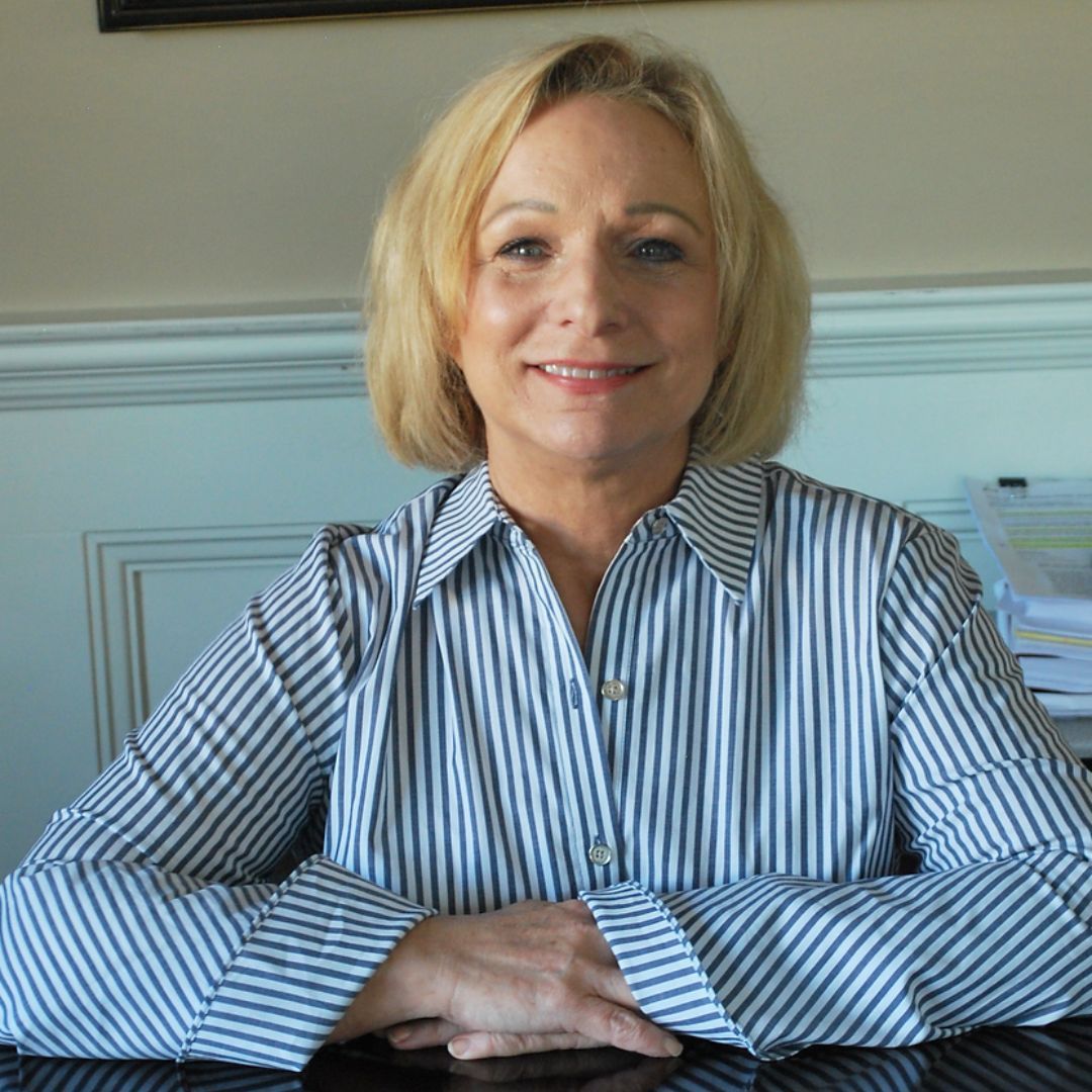 Jackie Findley in a striped shirt sits at a table with her hands folded