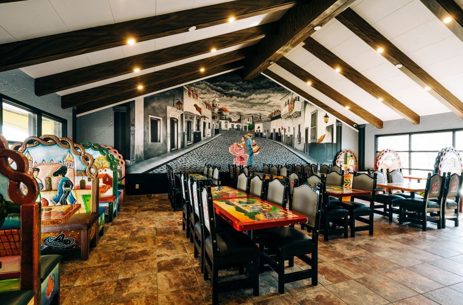 Restaurant interior with a large mural of a street scene and colorful tables and chairs.