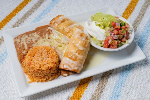 Two people grate cheese onto a pizza, kitchen setting.