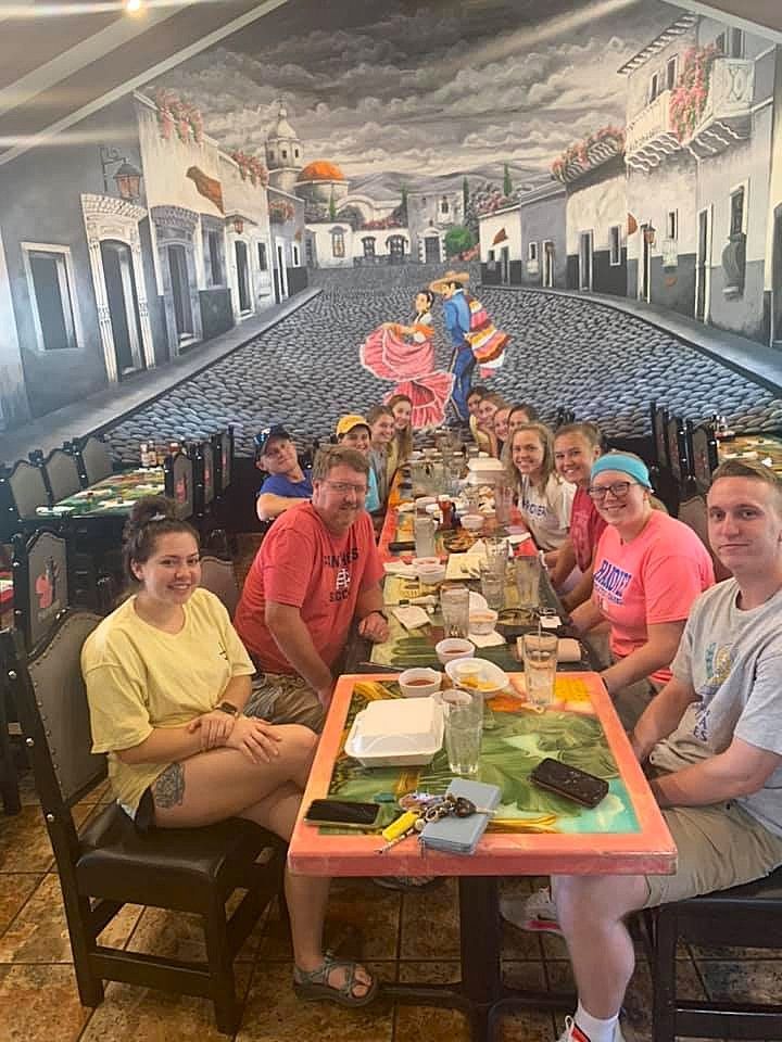 Group of people seated at a long table in a restaurant with a mural of a street scene behind them.