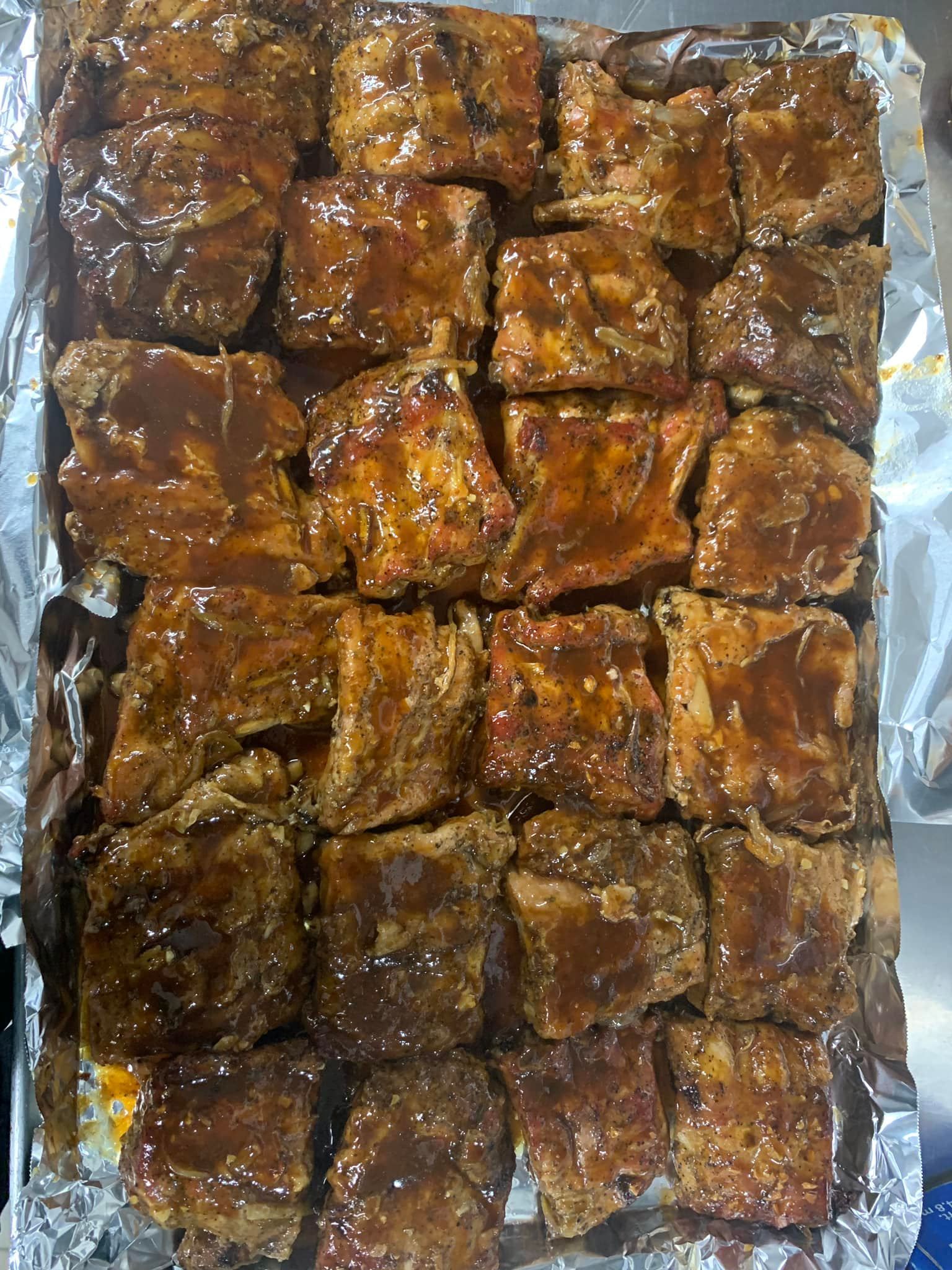 Tray of cooked, glazed ribs on foil. Brown, with visible spices and sauce.