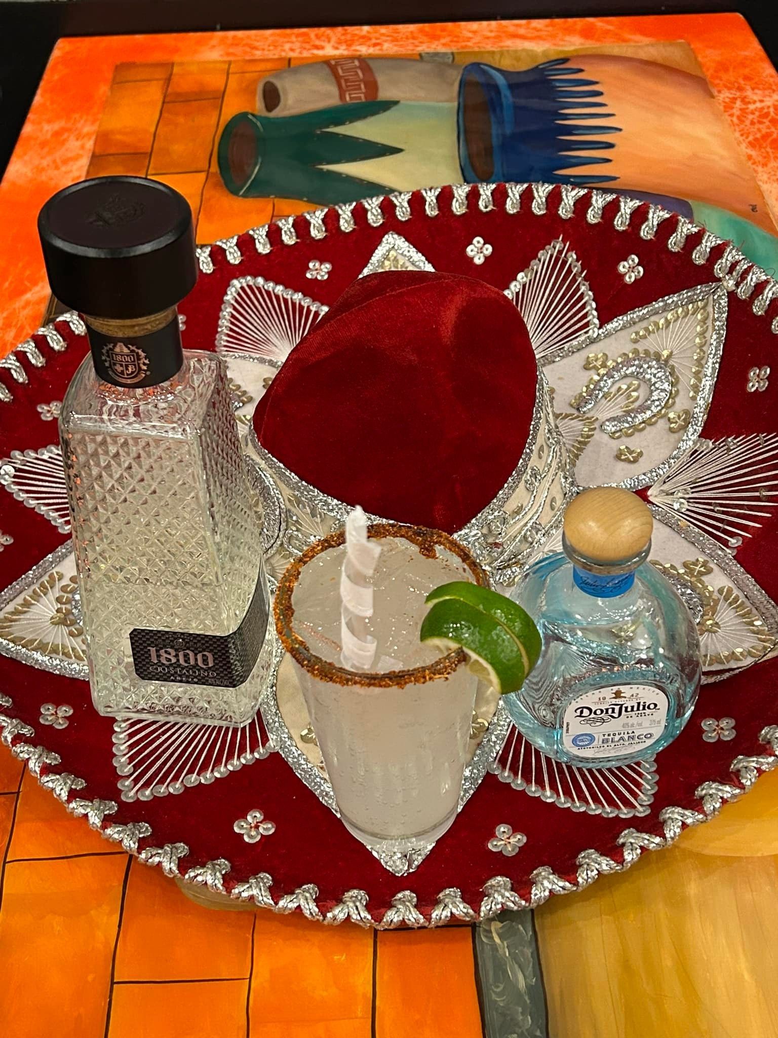 Tequila, margarita, and strawberry on a sombrero-shaped tray; vibrant colors, festive theme.