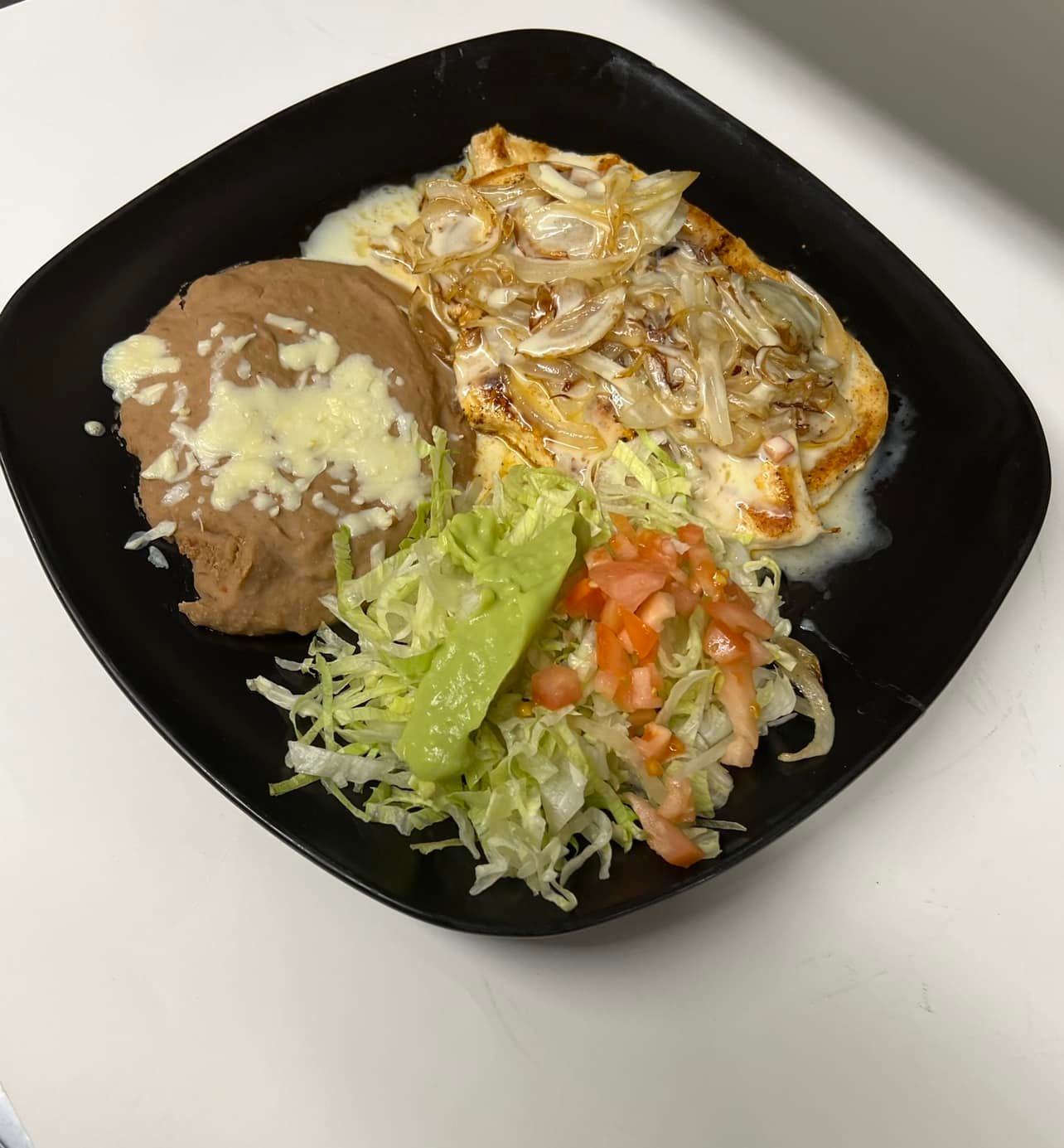 Plate of Mexican food with refried beans, salad, and a chicken dish covered in onions.