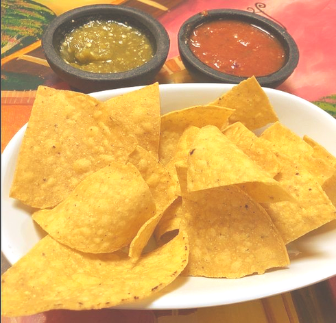 Tortilla chips in a white bowl with salsa verde and roja in black bowls.