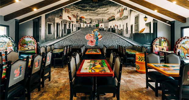 Restaurant interior with a large mural of a street scene and colorful tables and chairs.