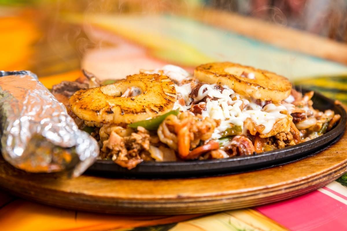 Sizzling fajitas with grilled pineapple and cheese on a hot plate, served with wrapped tortillas.