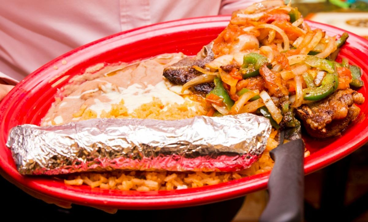 Red plate with burrito, rice, beans, and fajita vegetables.