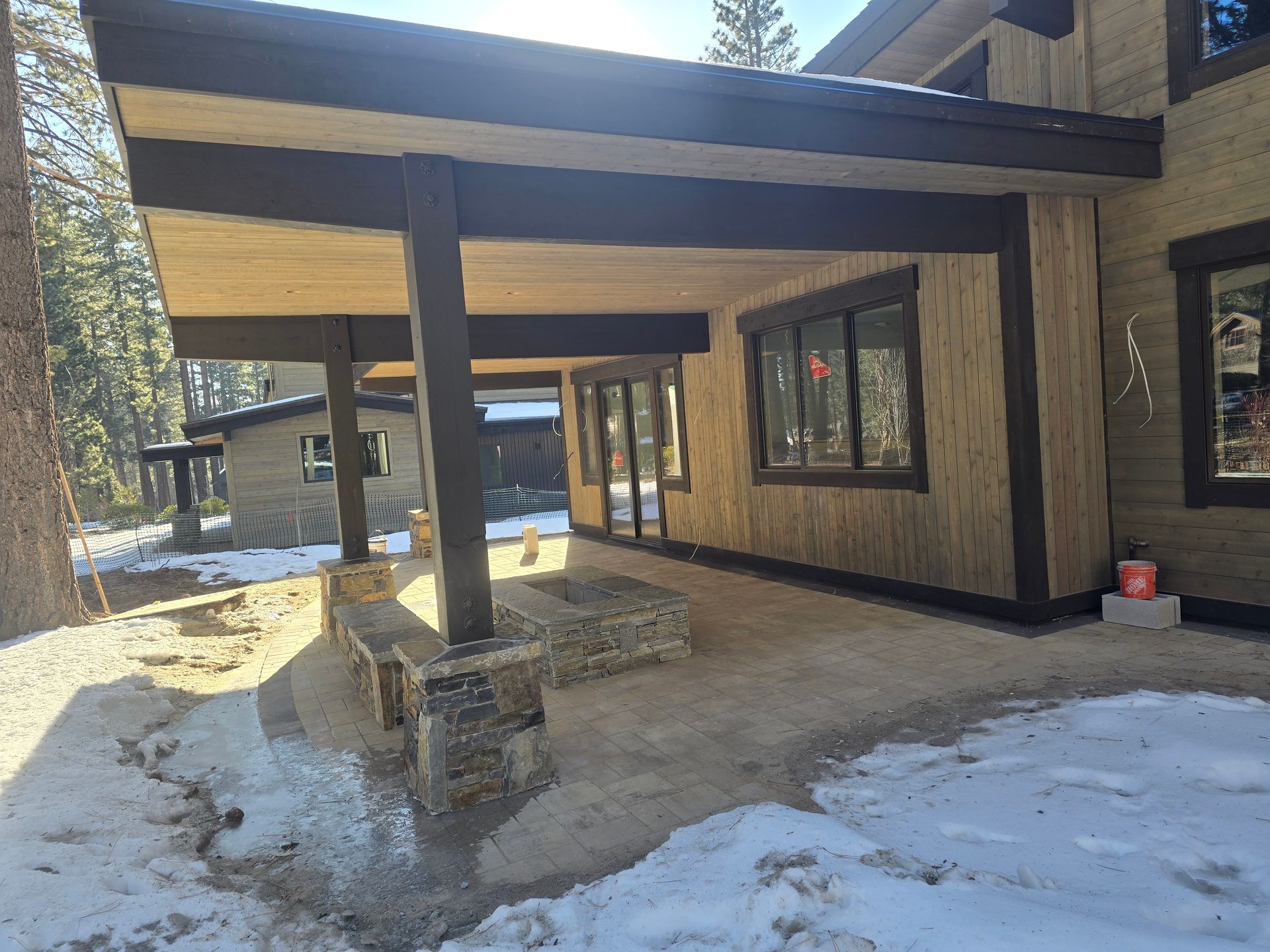 Modern house entry with covered porch, wood siding, stone columns, and snow on the ground
