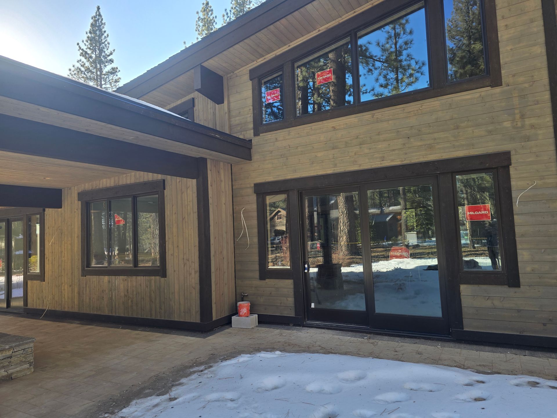 Modern two-story house exterior with large windows and sliding glass doors, snowy ground in front