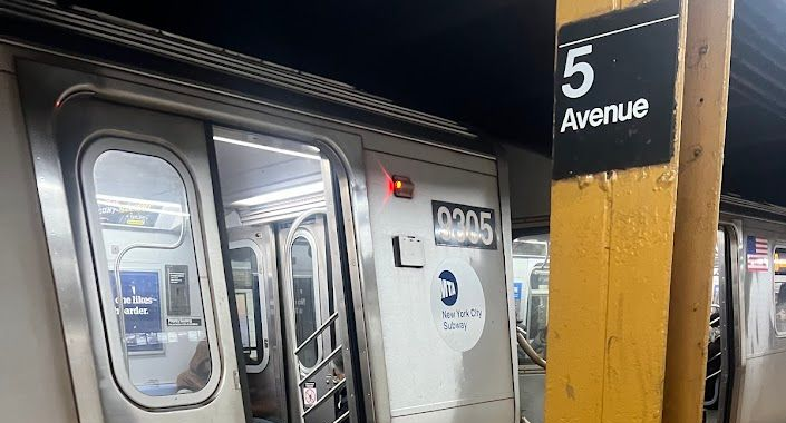Subway train at the 5th Avenue station. The doors are open. A yellow support pole is on the right.