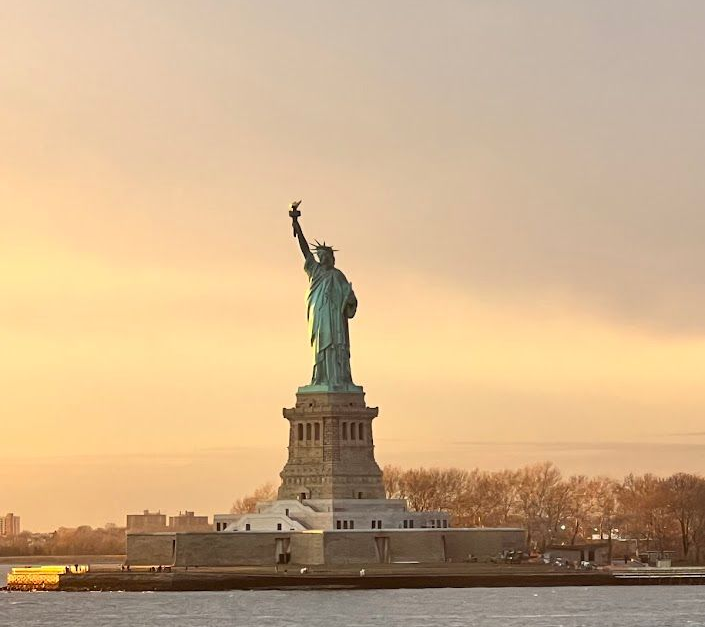 Statue of Liberty silhouetted against a golden sunset sky.