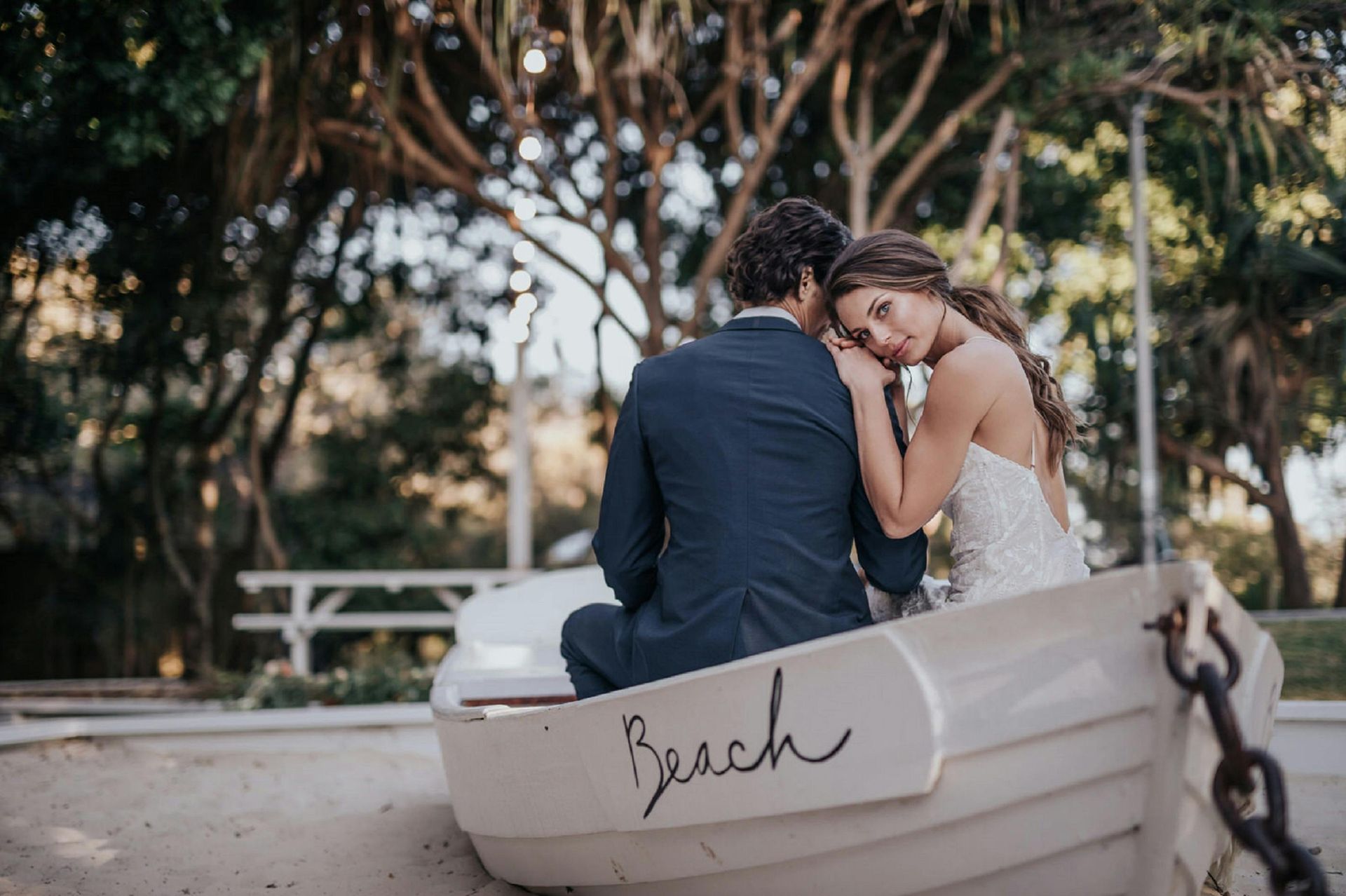Bride and groom sit in a small boat. The bride rests her head on the groom's shoulder.