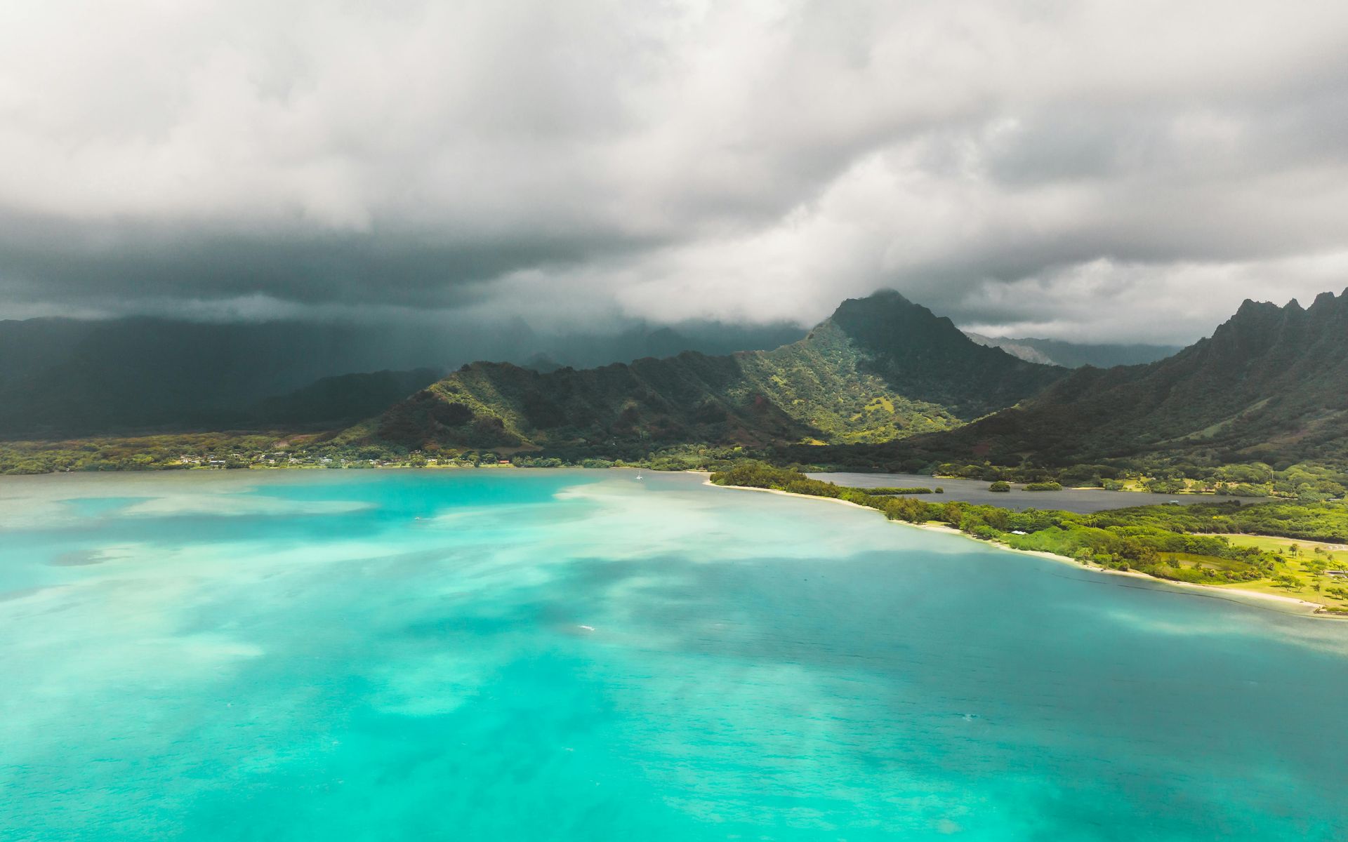 Turquoise lagoon under cloudy sky, with green mountains in the background.