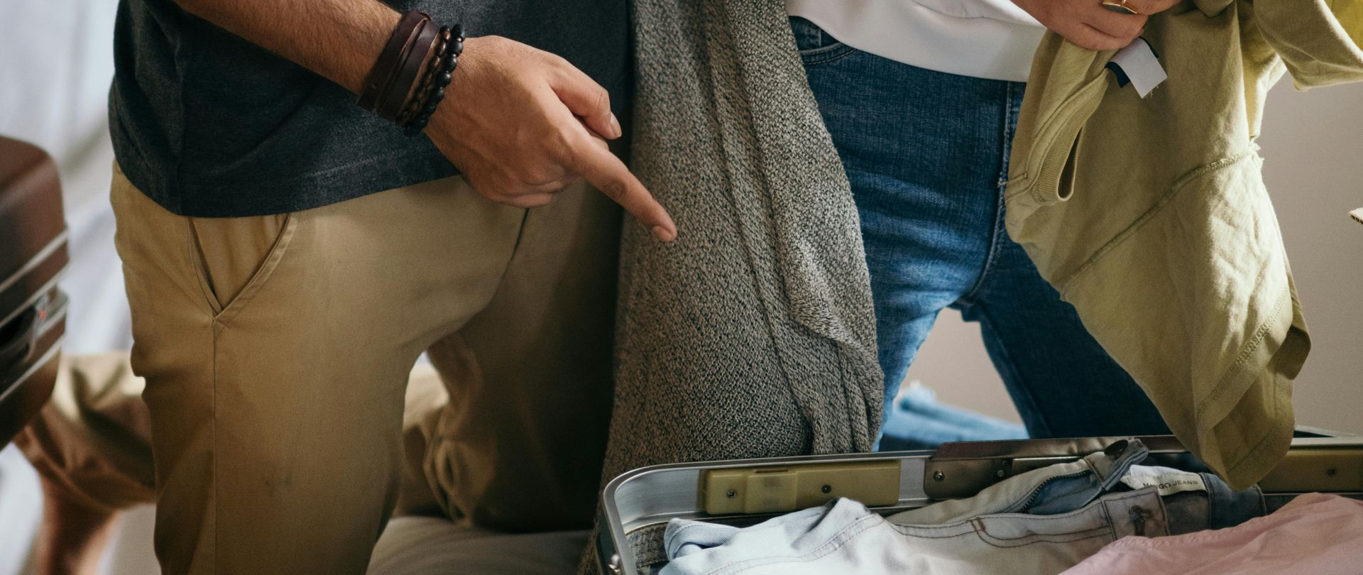Two people packing clothes into an open suitcase on a bed.