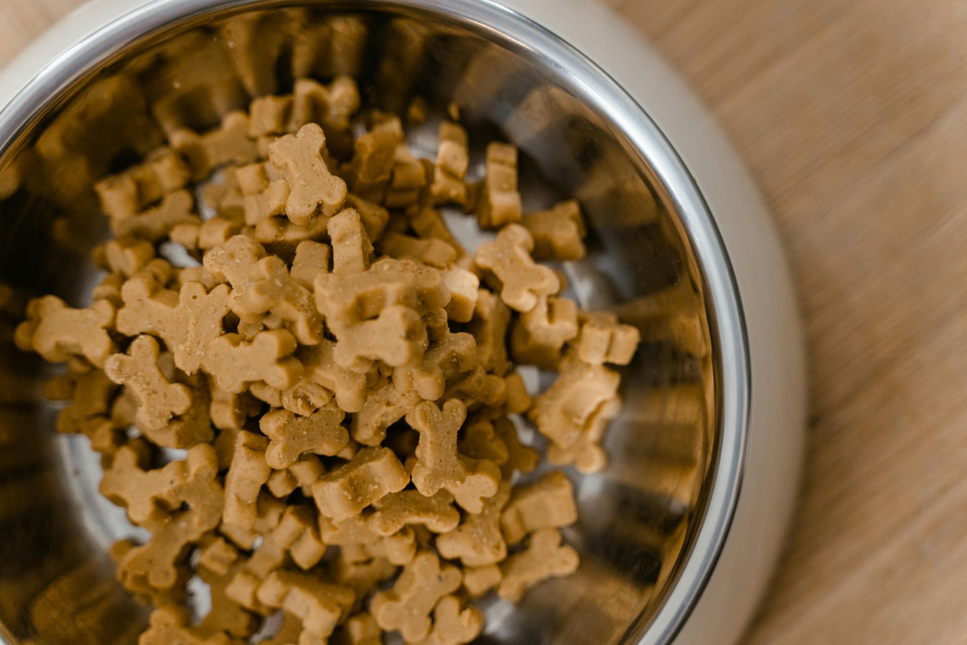 Dog biscuits in a silver bowl, on a light wood surface.