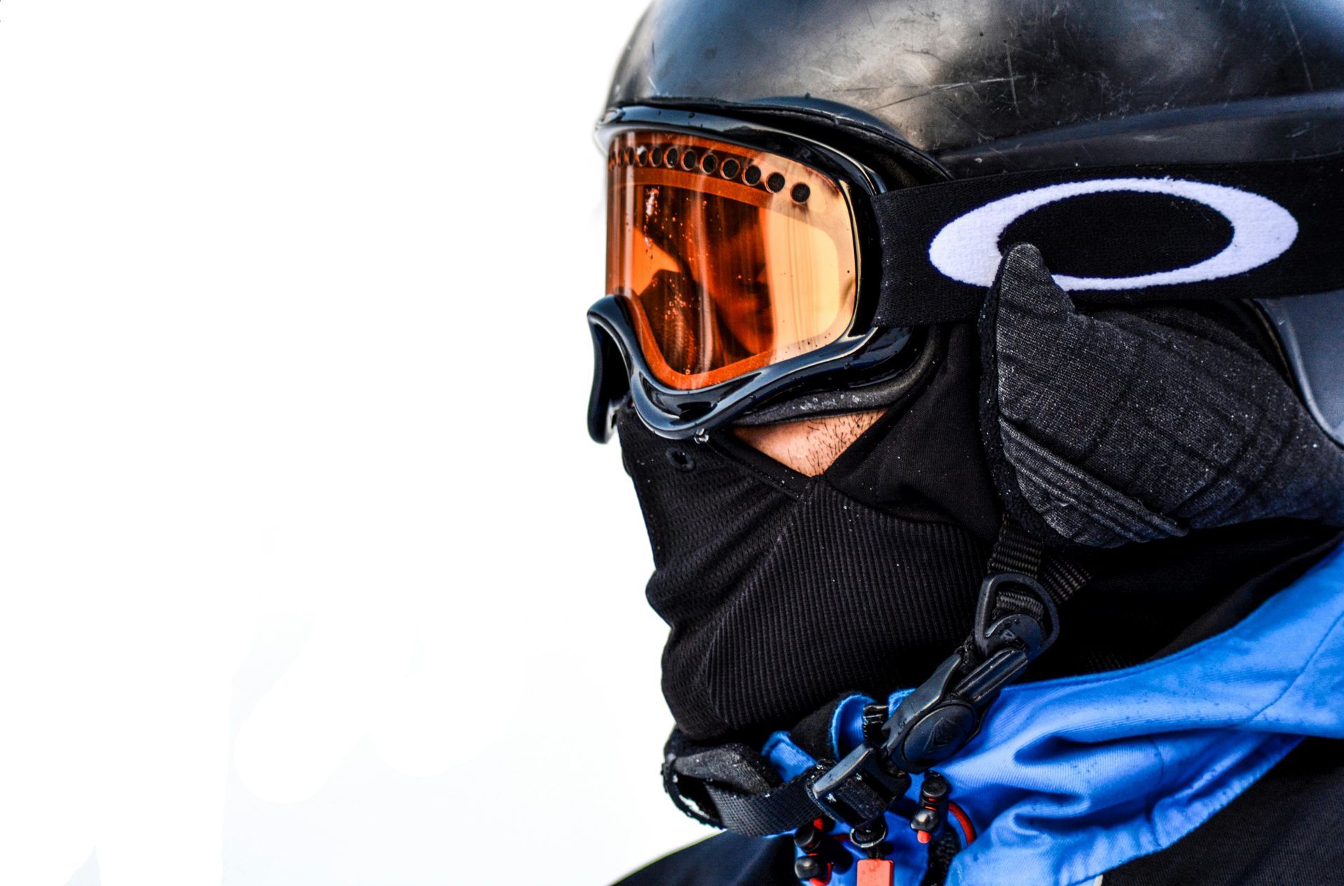 Person in black helmet and goggles, wearing a black face covering and blue jacket.