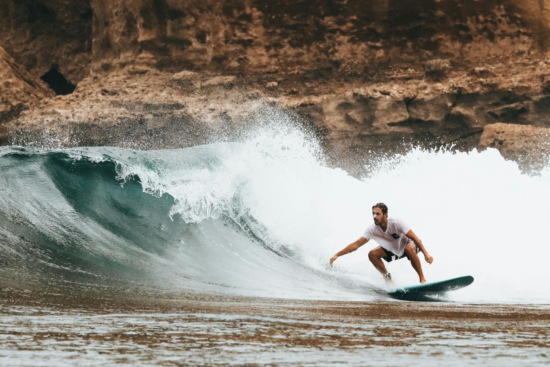 Surfer carving a wave near a rocky shore, water splashing.