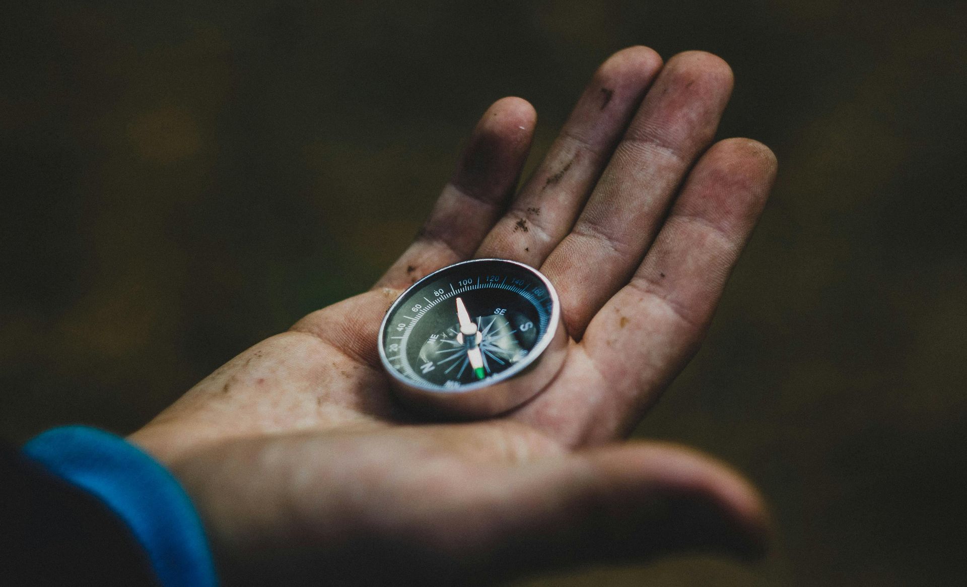 Hand holding a compass outdoors, guiding direction.
