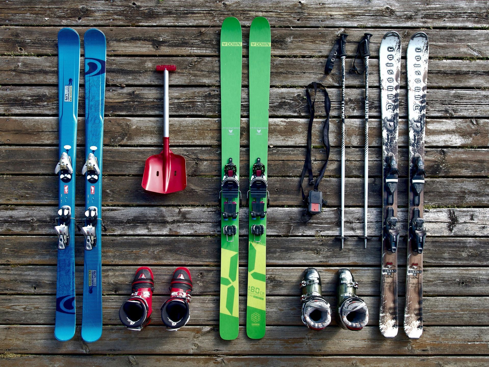 Ski gear arranged on weathered wooden planks: skis, boots, poles, and a shovel.
