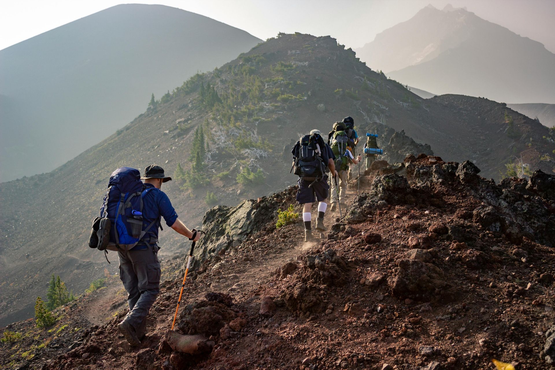 Hikers with backpacks climb a rocky mountain ridge on a sunny day.