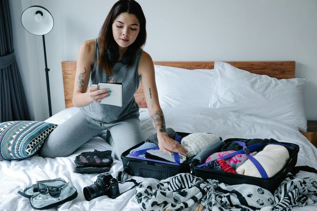 a woman sitting on her bed while packing her suitcase using her packing list to stay organized