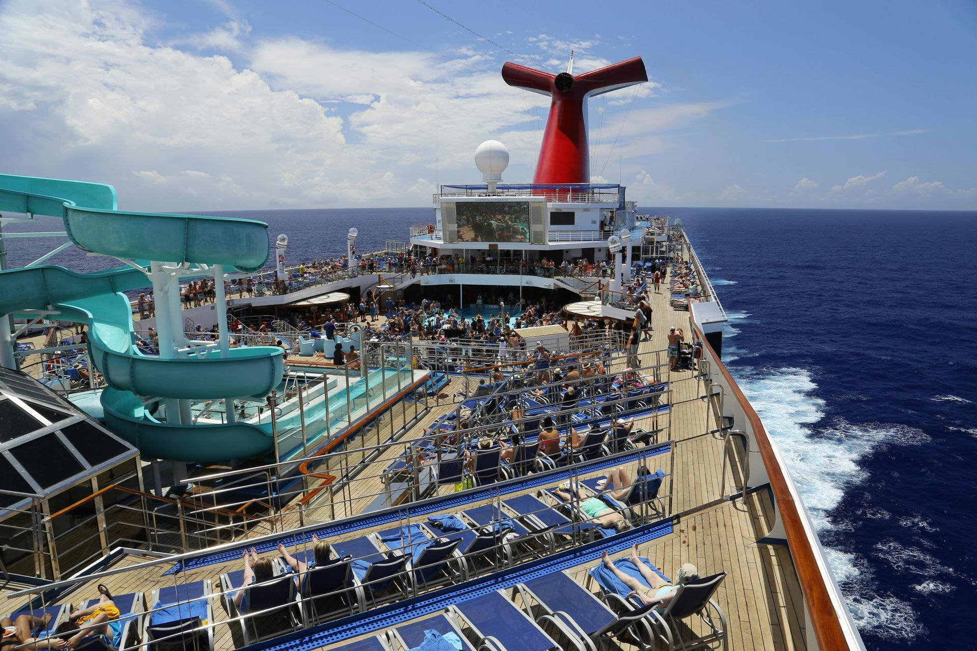 Cruise ship deck with people sunbathing, water slides, and the iconic Carnival funnel.
