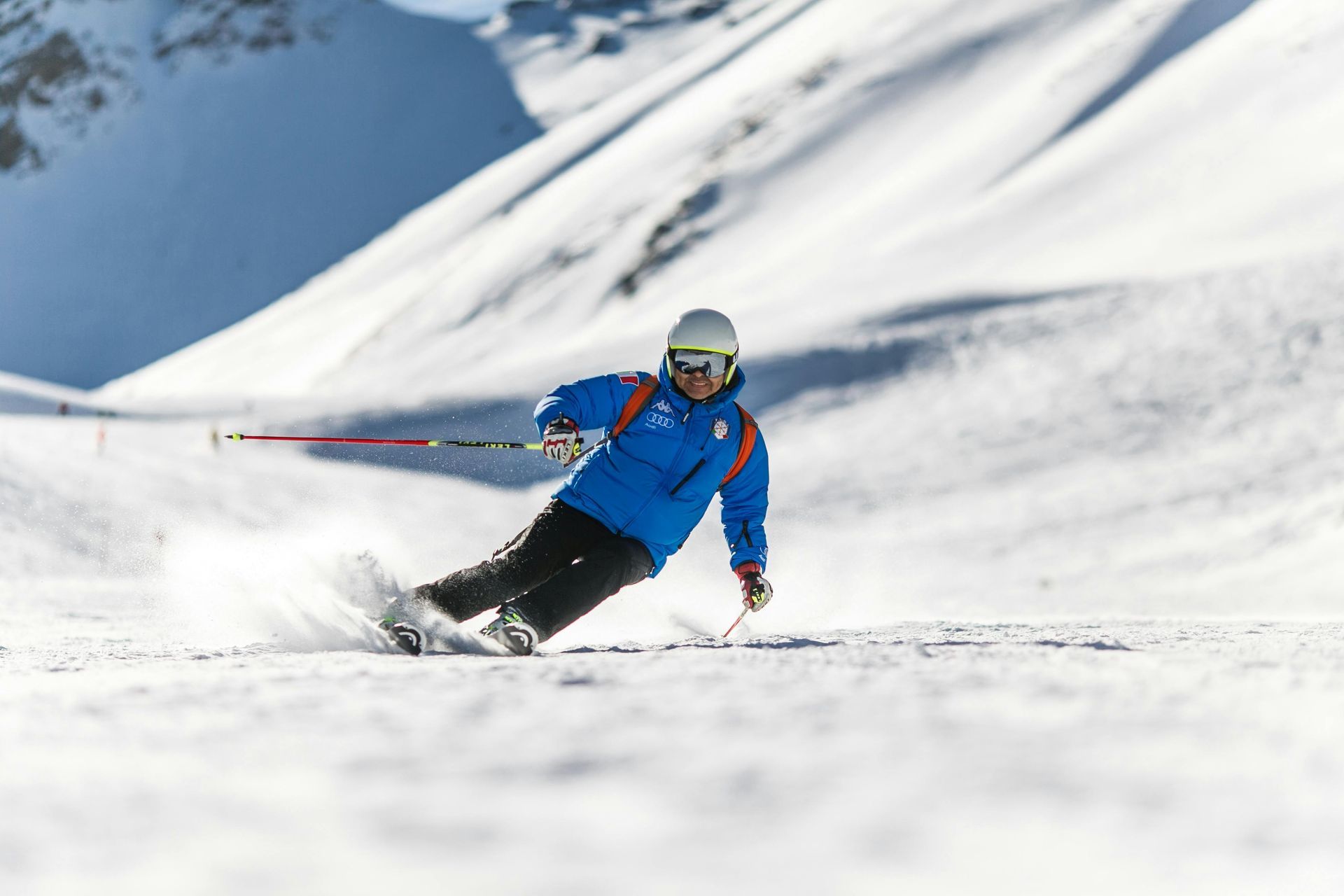 Skier in blue jacket carves down a snow-covered slope on a sunny day.